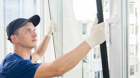 Un jeune professionnel en tenue de travail installe du double-vitrage sur la fenêtre d'un appartement
