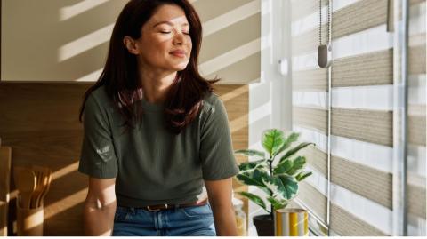 Femme profitant du soleil du matin à la maison près des stores de fenêtre 