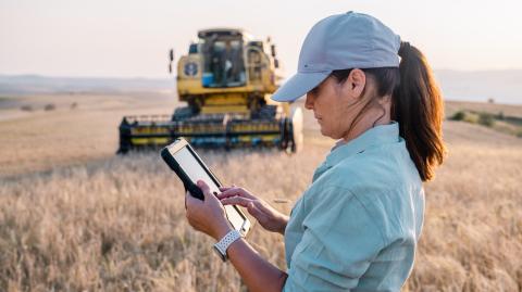 Une agricultrice tient une tablette numérique dans un champ agricole pour piloter son activité