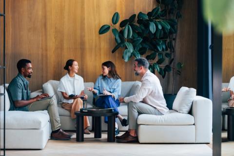 Quatre personnes discutant, assises sur des canapés gris. 