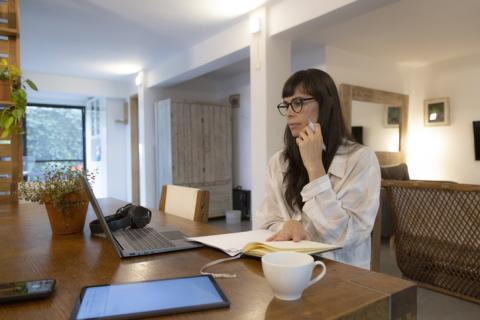 Femme brune travaillant sur son bureau, avec son ordinateur et une tasse de thé blanche.
