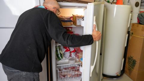Un homme cherche quelque chose dans son congélateur vertical, dans son garage
