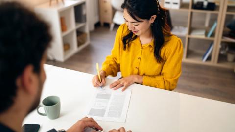 Une jeune femme d'origine asiatique aux cheveux longs signe un contrat lors d'un rendez-vous