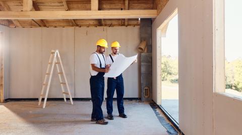2 artisans en tenue de travail étudient un plan dans une maison en construction