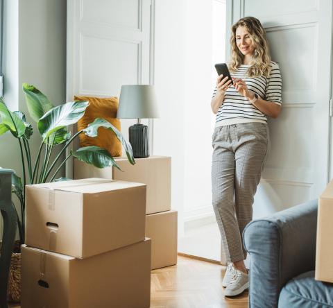 femme sur son téléphone dans un appartement entourée de cartons