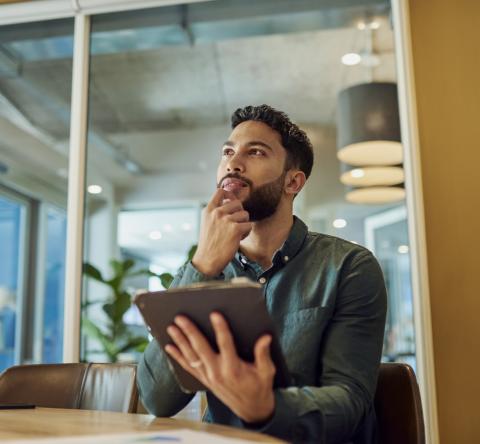 Un homme, réfléchissant, une tablette à la main