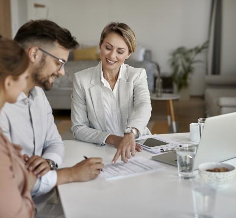 Un couple souriant signe le document que leur présente une femme.