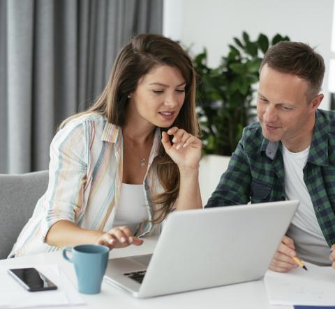 Un couple, installé autour d'une table de salon, étudie un dossier sur son ordinateur