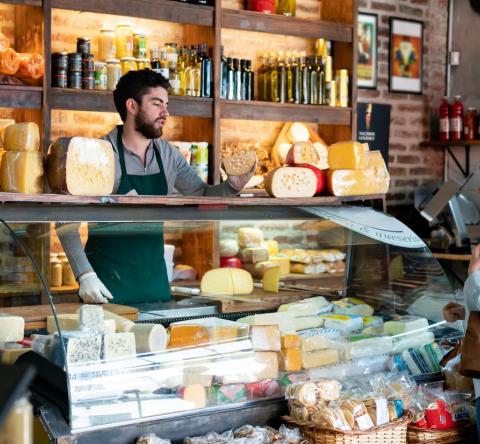 Un homme, debout derrière son comptoir, sert une cliente de sa fromagerie