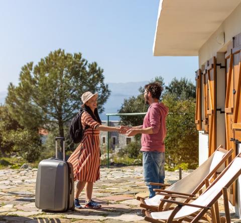 Un propriétaire accueille sa locataire, qui arrive avec sa valise pour un séjour de courte durée dans sa maison