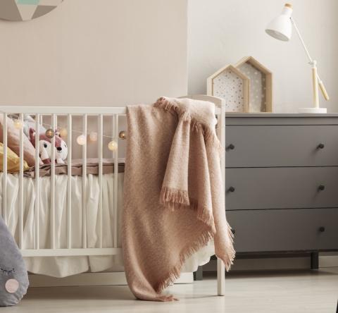 Une chambre d'enfant dans les tons roses avec un lit de bébé et une commode grise