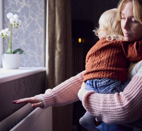 Une maman tenant son bébé dans les bras passe la main au-dessus du chauffage mural pour voir s'il fonctionne