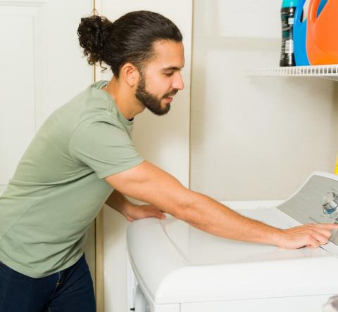 Un jeune homme d'origine hispanique programme son lave-linge dans sa buanderie