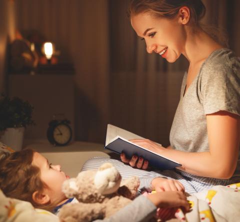 Une maman, assise sur le lit de son petit garçon, lui lit une histoire avant qu'il s'endorme