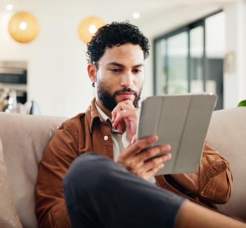 Un homme assis sur son canapé consulte des informations sur une tablette
