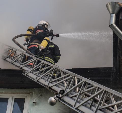 Un pompier professionnel projette un produit avec sa lance pour éteindre un incendie dans un logement depuis une échelle d'intervention