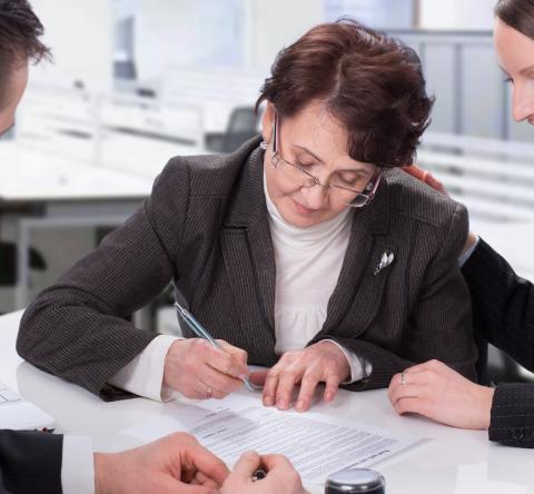 Une femme âgée signe un document officiel chez le notaire