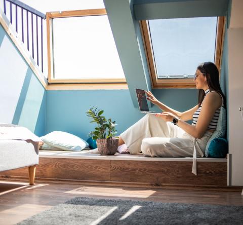 femme regarde son ordinateur portable installée sous son velux securisé