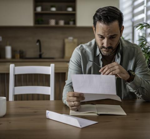 Un homme lit, préoccupé, le contenu d'un courrier qu'il vient de recevoir
