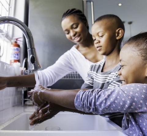 Une maman aide ses deux enfants qui se lavent les mains ensemble au lavabo de la salle de bain