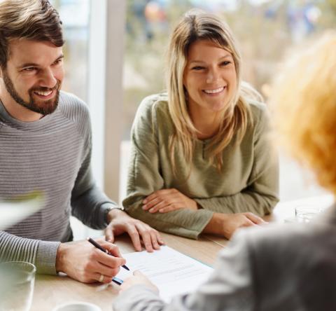 Un couple souriant valide les conditions d'un accord avec sa conseillère bancaire lors d'un rendez-vous