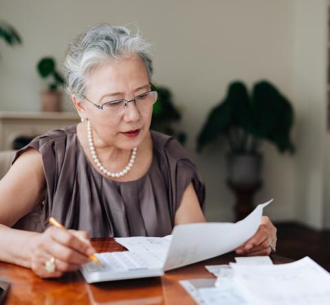 Une femme d'âge mûr vérifie ses factures sur sa table de salon, à l'aide de sa calculatrice