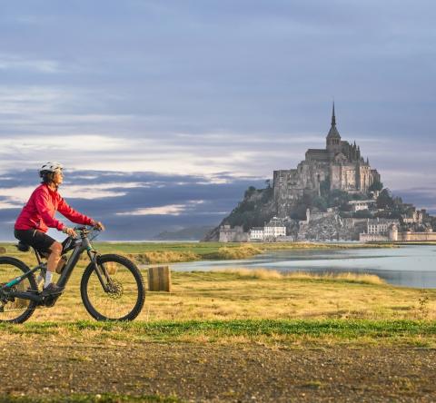 Touriste à vélo devant le Mont Saint-Michel, emblème de la Manche