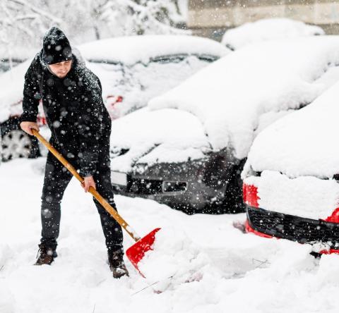 Un homme déneige le parking d'une copropriété à l'aide d'une pelle