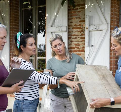 4 femmes échangent devant une maison en briques rouges au sujet des travaux en cours