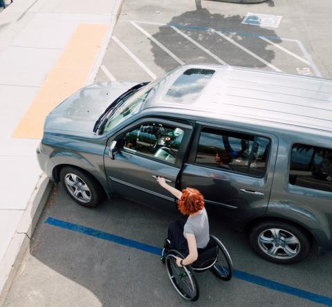 Une femme se déplaçant en fauteuil roulant ouvre la portière avant de son véhicule garé sur une place handicapé