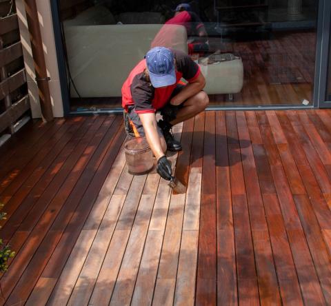 Un homme passe une couche de produit au pinceau sur une terrasse en bois pour la protéger et lui redonner de l'éclat