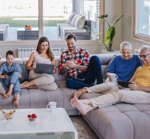 Une famille réunie sur le grand canapé d'angle gris qui consulte : ordinateurs et telephones...