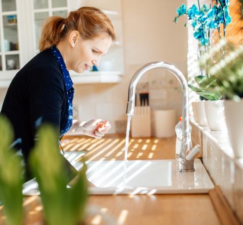 Une femme debout dans sa cuisine fait couler de l'eau dans son évier 