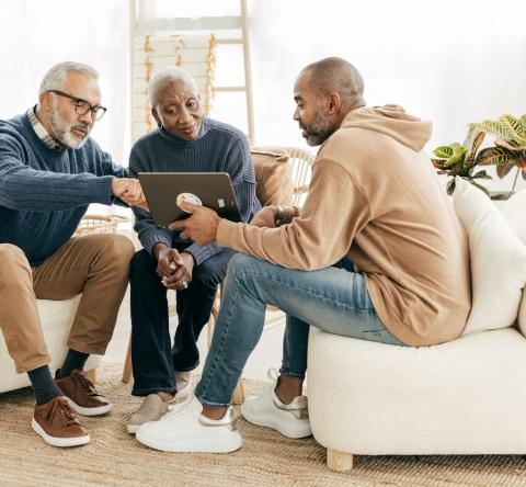 Un couple de personnes âgées échange avec un homme plus jeune et commente les informations fournies sur une tablette