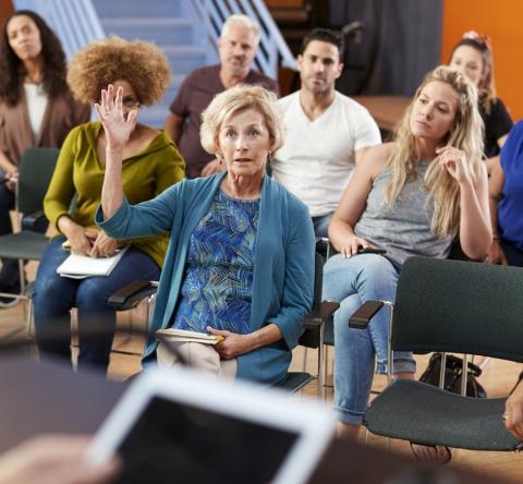 Une femme assise dans l'assemblée lève la main pour parler lors d'une assemblée générale de copropriété