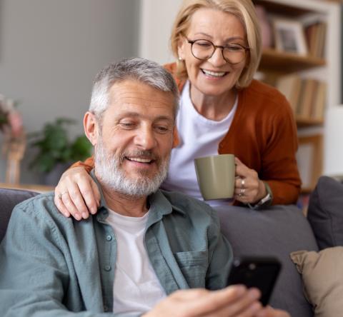 Un couple de retraités regarde des informations sur un téléphone portable dans son salon