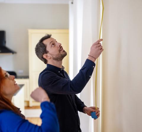 Un couple mesure la hauteur d'un mur de son logement à l'aide d'un mètre