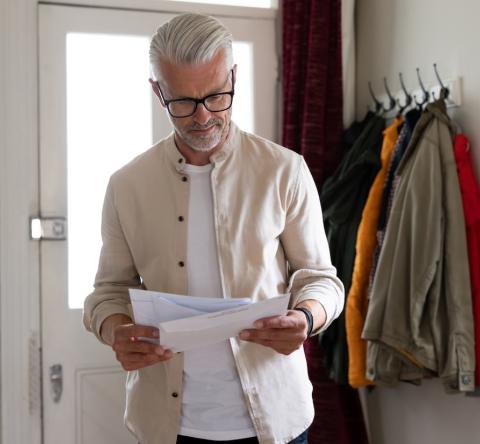 Un homme aux cheveux blancs lit un courrier qu'il vient de recevoir à son domicile
