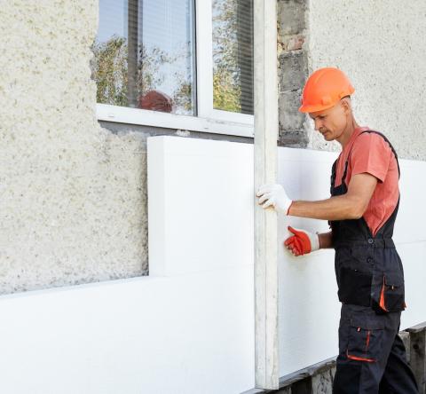 Un ouvrier du bâtiment réalise l'isolation extérieure d'une maison, en posant des panneaux isolants sur le mur extérieur