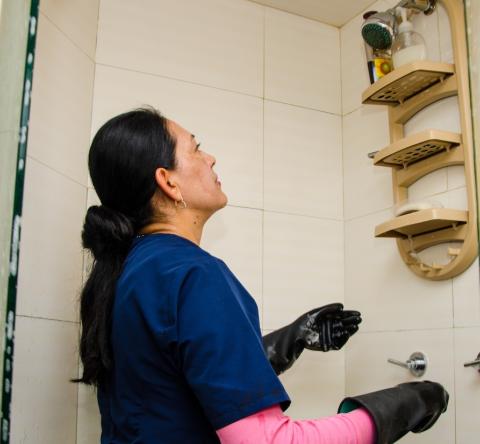 Une femme de ménage nettoie les murs carrelés d'une douche 