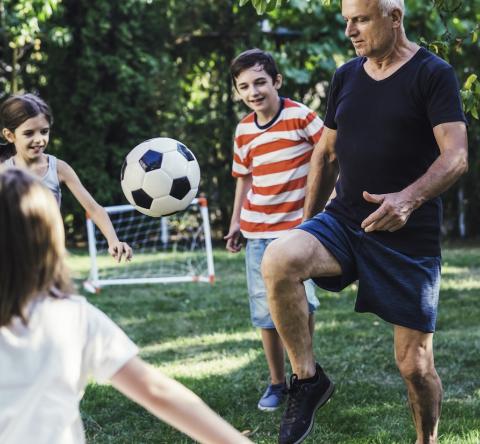 Des enfants jouent au foot dans leur jardin avec un homme d'âge mûr