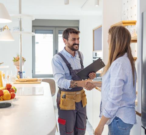 Une femme reçoit un ouvrier dans sa belle cuisine claire et lui serre la main. 