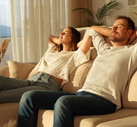 Un couple se détend, assis sur un canapé, les yeux fermés en profitant de la lumière du soleil