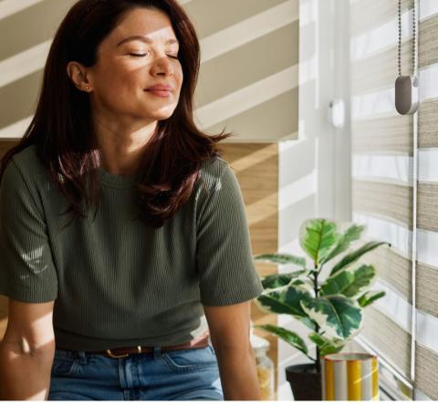 Femme profitant du soleil du matin à la maison près des stores de fenêtre 