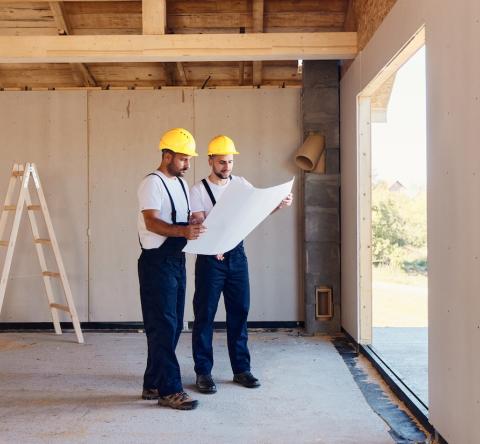 2 artisans en tenue de travail étudient un plan dans une maison en construction