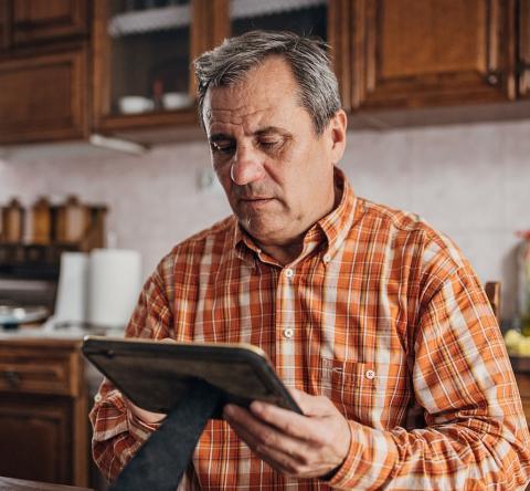 Un homme âgé se tient debout dans sa cuisine un peu ancienne, un cadre dans les mains